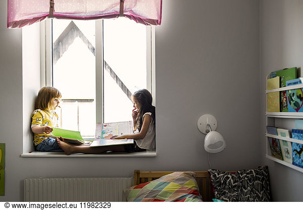 Girls (2-3  6-7) sitting and reading by window