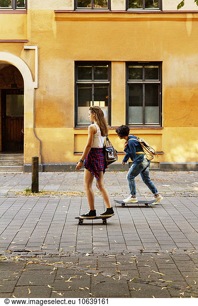 Girls skateboarding on street against building