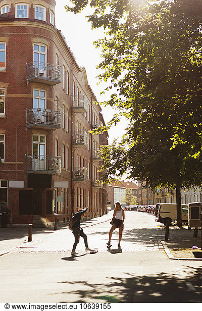 Girls skateboarding on street amidst buildings