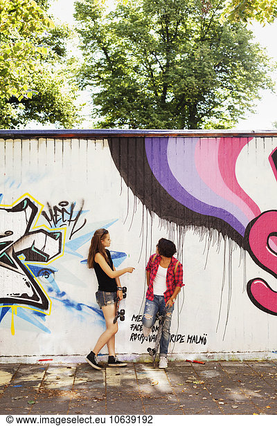 Girls standing on footpath against wall with graffiti