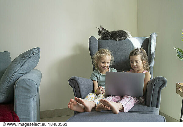 Girls watching laptop sitting in armchair at home