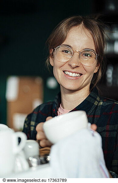 Glückliche Cafe-Besitzerin mit braunen Haaren beim Reinigen einer Kaffeetasse