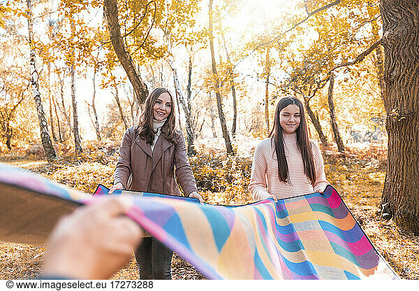 Glückliche Familie  die im Herbst im Park steht und eine Picknickdecke ausbreitet