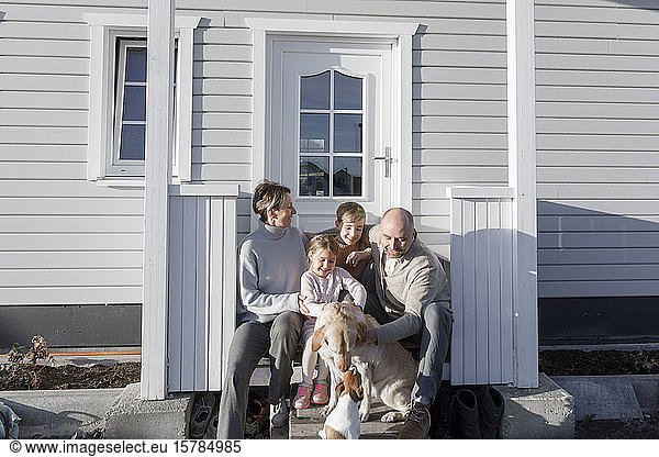 Glückliche Familie mit zwei Kindern und zwei Hunden  die vor ihrem Haus sitzen