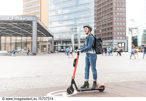 Glückliche Frau fährt E-Scooter in der Stadt  Berlin  Deutschland  Berlin  Deutschland