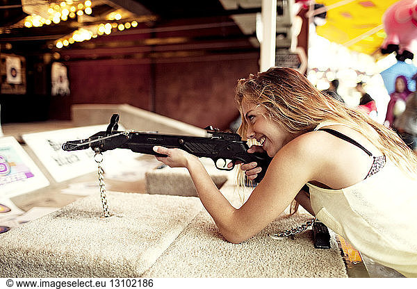 Glückliche Frau hält Gewehr am Jahrmarktstand