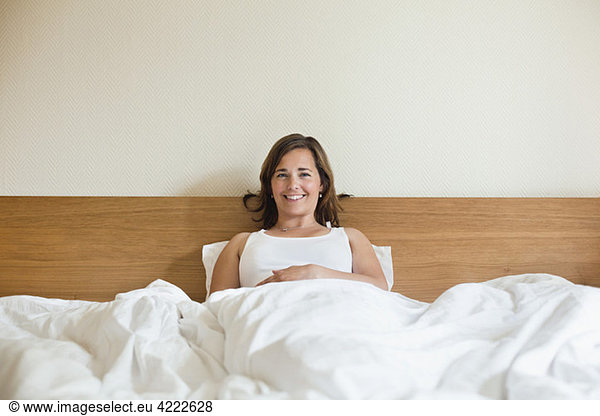 Glückliche Frau im Bett sitzend