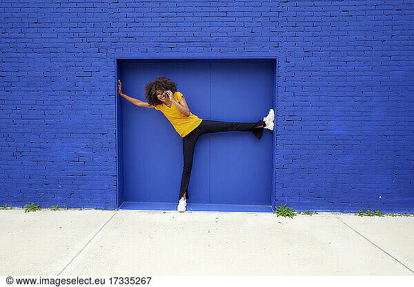 Glückliche Frau mit Brille  die sich vor einer blauen Wand streckt