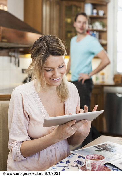 Glückliche Frau mit digitalem Tablett und im Hintergrund stehendem Mann in der Küche