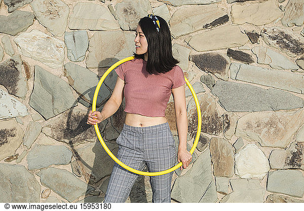 Glückliche Frau mit Hula-Hoop-Reifen vor einer Wand