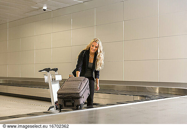 Glückliche Frau nimmt Gepäck vom Förderband