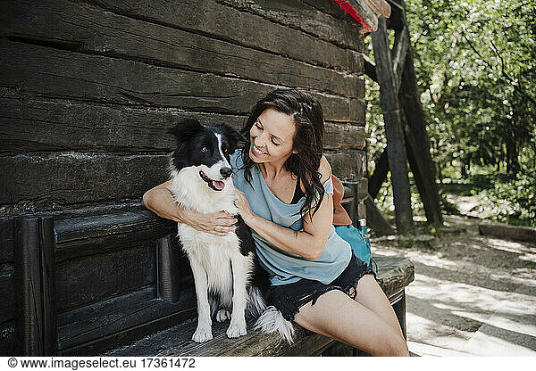 Glückliche Frau sieht ihren Hund an  während sie vor einem Haus sitzt und den Arm um ihn legt
