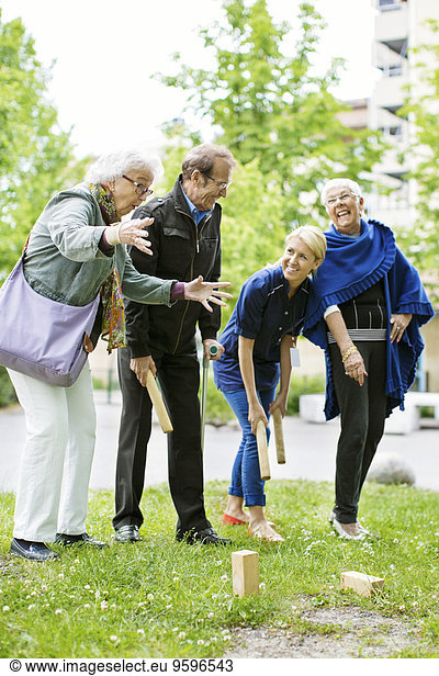 Glückliche Frau spielt Kubb Spiel mit Senioren im Park