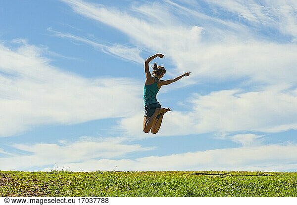 Glückliche Frau springt vor Freude  feiert den Sieg und genießt das Glück der Freiheit und unbeschwerten Lebensstil auf grünem Gras mit blauem Himmel  Hintergrund mit Kopie Raum