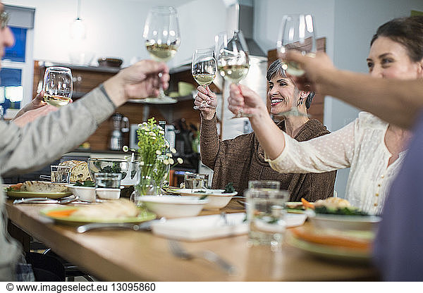 Glückliche Freunde stoßen bei geselligem Beisammensein am Tisch auf Wein an