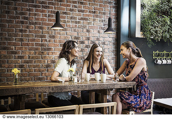 Glückliche Freunde trinken Kaffee bei Tisch an der Backsteinmauer im Café