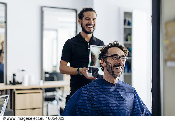 Glückliche Friseurin zeigt dem Kunden im Spiegel den Haarschnitt im Salon