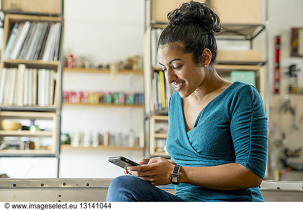 Glückliche Geschäftsfrau benutzt Smartphone  während sie im Büro sitzt