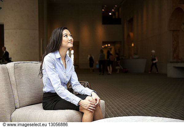 Glückliche Geschäftsfrau sitzt auf dem Sofa und schaut im Büro auf