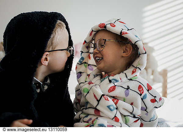 Glückliche Geschwister in warmer Kleidung  die sich gegenseitig im Schlafzimmer anschauen