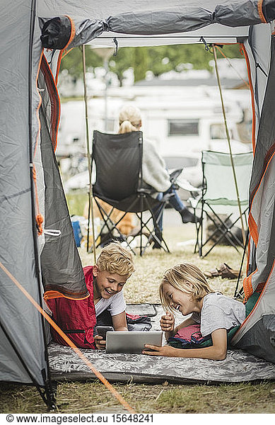 Glückliche Geschwister mit digitalem Tablet für Geschwister im Zelt auf dem Campingplatz