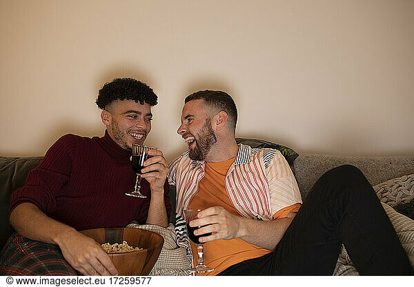 Glückliche Homosexuell männliches Paar trinken Rotwein und essen Popcorn zu Hause