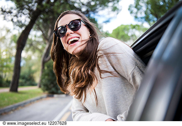 Glückliche junge Frau auf Autoreise lehnt sich aus dem Autofenster