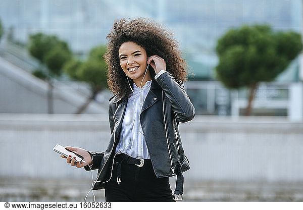 Glückliche junge Frau mit Afrofrisur  die im Freien stehend Musik hört