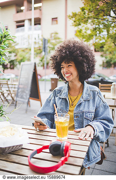 Glückliche junge Frau mit Afrofrisur in einem Straßencafé in der Stadt