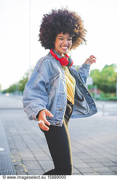 Glückliche junge Frau mit Afrofrisur tanzt in der Stadt