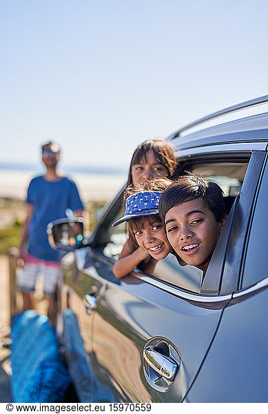 Glückliche Kinder lehnen sich auf einem Parkplatz am Strand aus dem Autofenster