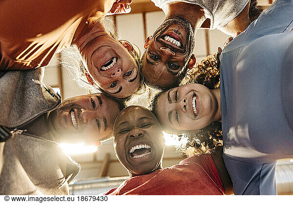 Glückliche männliche und weibliche Athleten lachen  während sie sich auf dem Sportplatz zusammenkauern