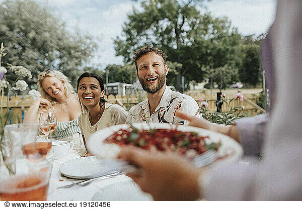 Glückliche männliche und weibliche Freunde lachen  während sie bei einer Dinnerparty am Tisch sitzen