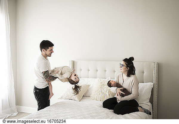 Glückliche Millennial-Familie spielt gemeinsam auf weißem Bett zu Hause