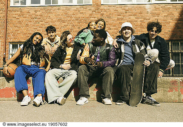 Glückliche multirassische männliche und weibliche Freunde sitzen vor einem Gebäude an einem sonnigen Tag