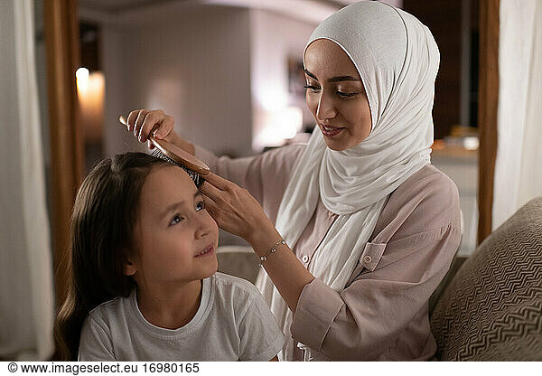 Glückliche muslimische Mutter frisiert ihre Tochter