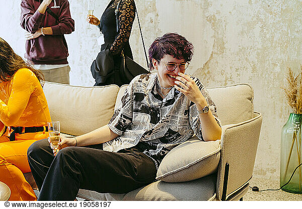 Glückliche nicht-binäre Person  die während einer Veranstaltung im Kongresszentrum auf dem Sofa sitzt und lacht