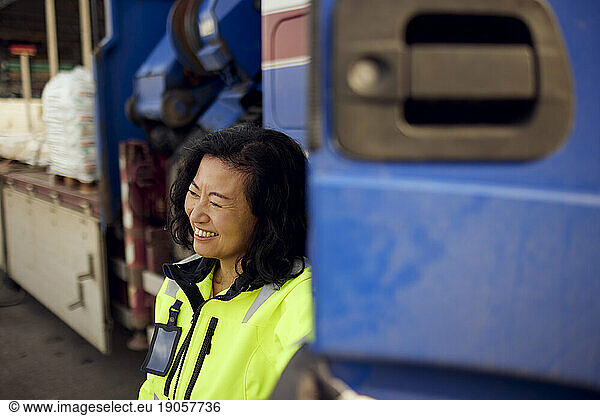 Glückliche reife Arbeiterin steht bei einem Lastwagen in der Industrie