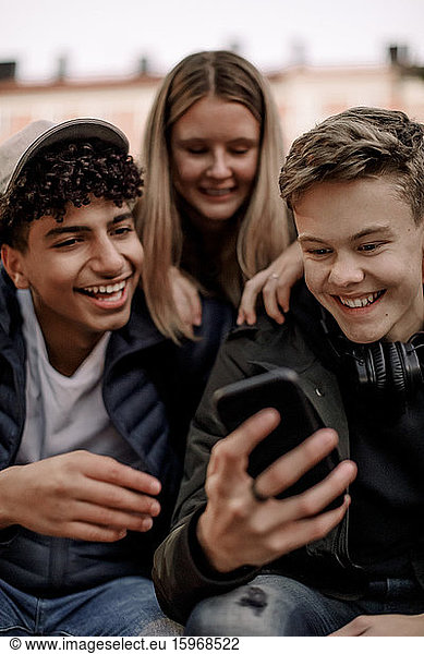 Glückliche Teenager nutzen soziale Medien auf dem Mobiltelefon  während sie in der Stadt sitzen