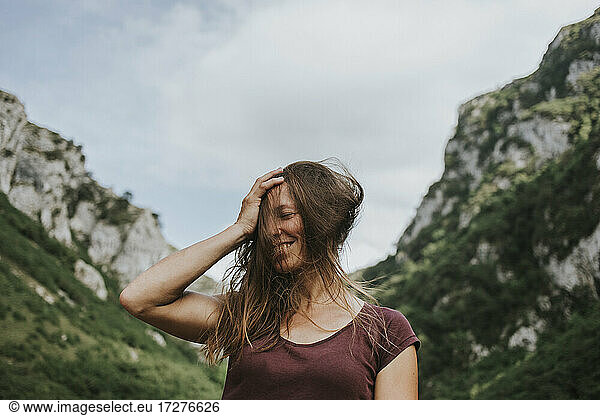 Glückliche Wanderin mit zerzausten langen braunen Haaren vor einer Bergkette