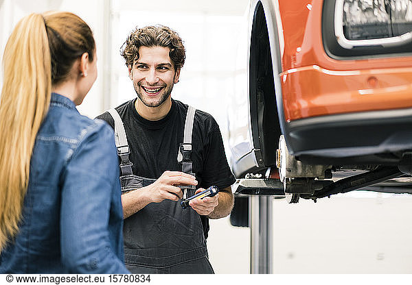 Glücklicher Automechaniker im Gespräch mit Kunden in der Werkstatt