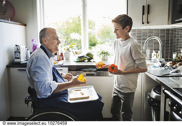 Glücklicher behinderter Vater im Rollstuhl bei der Zubereitung des Essens mit Sohn in der Küche