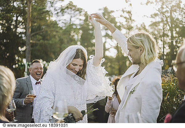 Glücklicher Bräutigam hält die Hand der Braut und tanzt inmitten der Gäste bei einer Hochzeitsfeier