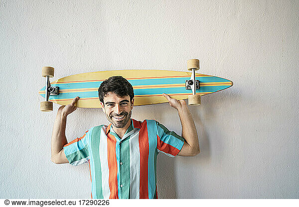 Glücklicher gut aussehender Mann mit Longboard vor einer Wand
