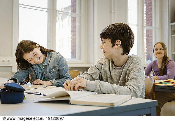 Glücklicher Junge lacht  während seine Freundin am Schreibtisch im Klassenzimmer sitzt
