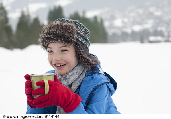 Glücklicher Junge trinkt heiße Schokolade im verschneiten Feld