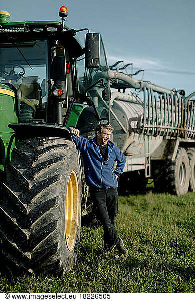 Glücklicher reifer Landwirt mit Traktor auf dem Feld stehend