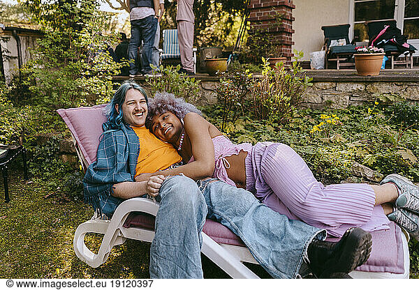 Glücklicher schwuler Mann mit Transfrau auf einem Stuhl liegend während einer Party im Hinterhof