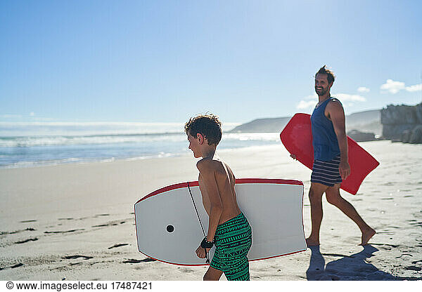 Glücklicher Vater und Sohn mit Bodyboards am sonnigen Sommerstrand