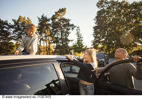 Glücklicher Vater und Tochter beim Anblick des Jungen auf dem Autodach